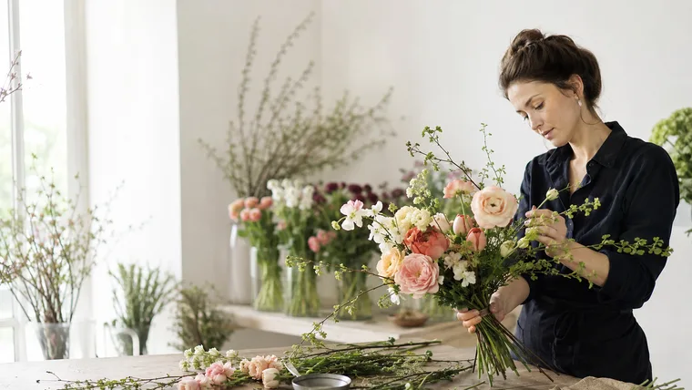 Floristin bindet einen Strauß mit Rosen und Ranunkeln (Konzeptstudie Blüte & Zweig)